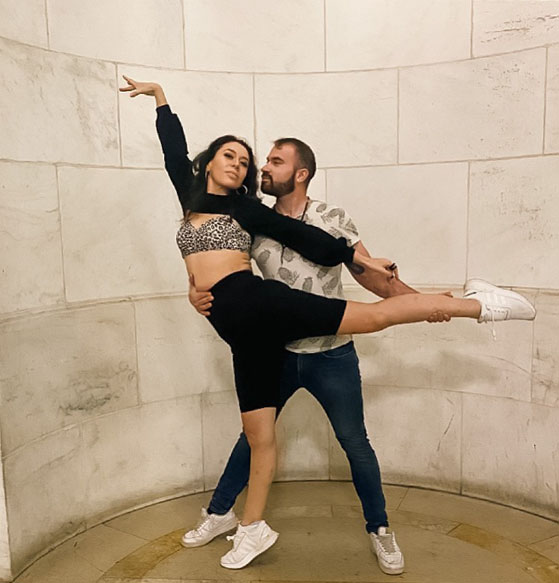 Mariela dancing, with arm and leg raised, supported by dance partner